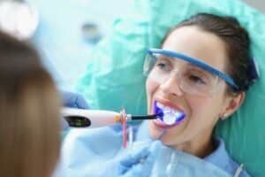Patient undergoing professional teeth whitening treatment at a dental clinic, with protective gear and whitening device in place.