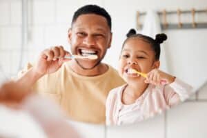 A father and daughter brushing their teeth with manual toothbrushes