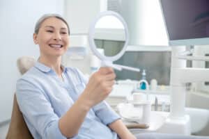 Woman looking in the mirror after having a missing tooth replaced in Houston